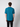 A man with short, curly brown hair faces away from the camera, wearing a teal PROJEK RAW Mens Short Sleeve Crew T-shirt and black pants against a plain light gray background.