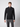 A person stands against a plain light background, wearing a black PROJEK RAW Mens Half-zip Cashmere Touch Sweater and gray plaid pants, looking directly at the camera with a neutral expression.