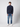 A young man stands against a plain light background, wearing a PROJEK RAW Mens Zip Mock Neck Sweater in navy, paired with light blue jeans and white sneakers. He looks straight ahead with a neutral expression.