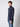 A young man with curly brown hair wears a PROJEK RAW Mens Zip Mock Neck Sweater in navy blue and blue jeans, standing against a plain light gray background and looking slightly to the side.