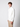 A young man with curly brown hair wears a white PROJEK RAW Mens Zip Mock Neck Sweater and beige pants, standing against a plain light gray background and looking calmly at the camera.