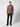 A young man stands in a studio against a plain light background, wearing the PROJEK RAW Mens Cable Knit Mock Neck Sweater in brown, paired with black pants and black shoes.