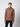 A young man stands against a plain light gray background, wearing the PROJEK RAW Mens Cable Knit Mock Neck Sweater in brown with black pants. He is facing forward with a neutral expression.