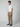 A man with short curly hair and a neutral expression stands against a plain background, wearing PROJEK RAW’s Mens Solid Bungee Cargo Pant in tan, paired with a white t-shirt and black slip-on shoes for an effortless streetwear look.