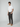 A man stands against a plain background wearing a white short-sleeve t-shirt, PROJEK RAW Mens Solid Bungee Relaxed Chino Pant in dark gray, and light brown shoes. He looks forward with one hand in his pocket and the other by his side.