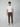 A man with curly hair wears a plain white t-shirt, beige loafers, and PROJEK RAW Mens Solid Bungee Fashion Chino Pant in brown, standing against a neutral gray background.