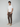 A man stands against a plain light background, wearing a white t-shirt, beige slip-on shoes, and PROJEK RAW Mens Solid Bungee Fashion Chino Pant in brown with a tailored fit. One hand is in his pocket, and he looks forward neutrally.