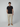 A man with short dark hair wears PROJEK RAW Mens Bungee Loose Cargo Pant, a black T-shirt, and tan suede shoes against a plain light gray background. He has a neutral expression and one hand in his pocket.
