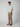 A person stands in a neutral pose against a plain background, wearing a light blue short-sleeve shirt, PROJEK RAW Mens Solid Bungee Relaxed 5-Pocket Pant with an elastic waistband, brown slip-on shoes, hands in pockets, looking at the camera.