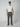 A man wears PROJEK RAW Mens Solid Bungee Loose Chino Pant, a white t-shirt, brown slip-on shoes, and a brown cap against a plain background. He looks straight at the camera with a neutral expression.