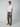 A man stands against a plain background wearing PROJEK RAW Mens Solid Bungee Loose Chino Pants, a white t-shirt, brown slip-on shoes, and a brown baseball cap. His hands are by his sides and his expression is neutral.