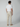A man stands with his back to the camera, wearing a plain white T-shirt, beige PROJEK RAW Mens Drawstring Chino Pant, and beige shoes against a plain gray background.