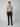 A young man with short brown hair and a neutral expression stands facing forward against a light gray background, wearing PROJEK RAW MENS 5-POCKET PANT, a beige short-sleeve polo shirt, tan belt, and black loafers.