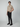 A young man stands against a plain background wearing a beige short-sleeve polo, PROJEK RAW MENS 5-POCKET PANT with a matching belt, and black shoes, one hand in his pocket.