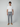 A man stands facing forward, wearing a plain white t-shirt, PROJEK RAW MENS 5-POCKET PANT in light gray, and tan sneakers against a simple light gray background.