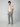 A man stands against a plain light background, wearing PROJEK RAW Mens Drawstring Linen Pant in gray with a beige short-sleeve shirt over a white T-shirt and beige loafers. One hand is in his pocket as he looks toward the camera.