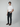 A man stands against a plain background, wearing a white t-shirt, PROJEK RAW MENS 5-POCKET ATHLETIC FIT JEAN, and brown loafers. One hand is in his pocket as he looks at the camera with a neutral expression.