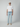 A young man stands facing forward against a light gray background, wearing a beige cap, plain white t-shirt, PROJEK RAW MENS 5-POCKET ATHLETIC FIT JEAN in light blue with stretch fabric, and beige slip-on shoes.