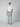 A man stands against a plain light gray background wearing a white T-shirt, PROJEK RAW MENS 5-POCKET ATHLETIC FIT JEAN, tan slip-on shoes, and a beige cap.