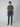 A young man stands against a plain background, wearing a short-sleeved olive green t-shirt and PROJEK RAW BARU MENS 5-POCKET JEAN in blue stretch denim, paired with brown boat shoes. He faces forward with a neutral expression and relaxed posture.
