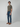 A young man in an olive green tee, brown boat shoes, and PROJEK RAW BARU MENS 5-POCKET JEAN in stretch blue denim stands against a grey background, turned slightly to the side with a neutral expression.