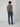 A person stands facing away, wearing an olive green short-sleeve T-shirt, PROJEK RAW BARU MENS 5-POCKET JEAN in stretch denim, and brown shoes, set against a plain light gray background.
