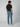 A person with brown hair, facing away, wears a black T-shirt, white sneakers, and PROJEK RAW NIKKO MENS 5-POCKET SLIM FIT JEAN in light blue against a plain light gray background.