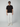 A man in black sunglasses, a black short-sleeve henley shirt, PROJEK RAW Mens 5-Pocket Regular Fit Denim, and white sneakers stands facing forward against a plain light gray background.