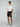 A young man stands against a light gray background, wearing a white short-sleeve shirt, PROJEK RAW Mens 5-Pocket Solid Bungee Shorts with an elasticized waistband, and gray sneakers. He faces forward with a neutral expression and relaxed posture.