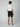 A man faces away from the camera, wearing a white short-sleeve shirt, PROJEK RAW Mens 5-Pocket Solid Bungee Shorts, and white sneakers against a plain light gray background.