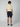 A person stands facing away, wearing a short-sleeve cream shirt, PROJEK RAW Mens 5-Pocket Solid Bungee Shorts, and navy slip-on shoes against a plain light background.