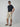 A man in dark sunglasses, a navy blue t-shirt, PROJEK RAW Mens Solid Bungee Pull-on Cargo Shorts, and brown sandals stands confidently with one hand in his pocket against a plain light gray background.