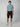 A man stands facing forward against a plain background, wearing a light blue t-shirt and PROJEK RAW Mens Solid Bungee Capri Cargo Shorts 13 Inseam, paired with white sneakers. His arms are by his sides and he has a neutral expression.