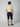 A man faces away from the camera, wearing a short-sleeved beige polo and PROJEK RAW Mens Solid Bungee Capri Cargo Shorts 13 Inseam with pockets, paired with navy slip-on shoes, set against a plain light gray background.