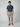 A man stands facing forward in a navy short-sleeve button-up shirt, PROJEK RAW Mens Texture Bungee 5-Pocket Short in beige, and brown boat shoes, set against a plain light gray background.