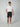 A man stands against a plain background wearing a white t-shirt, PROJEK RAW Mens Texture Bungee Chino Short 9 Inseam with a belt, and white sneakers. One hand is in his pocket as he faces forward—an effortless summer look.