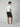 A man with his back turned wears a white t-shirt, PROJEK RAW Mens Texture Bungee Chino Short 9 Inseam, and white sneakers. One hand in his pocket, he glances over his shoulder—an easy summer look set against a plain light background.