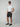 A man in black sunglasses, a plain white tee, PROJEK RAW MENS BUNGEE PLAID CHINO SHORTS made from stretch fabric, and black slip-on shoes stands against a light gray background with one hand in his pocket.