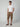 A man with a neutral expression poses against a plain background wearing a white t-shirt, brown sandals, and PROJEK RAW MENS CAPRI CARGO SHORT made from durable fabric, with one hand in his pocket.