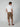 A man faces away, wearing a white t-shirt, brown PROJEK RAW MENS CAPRI CARGO SHORT made from durable fabric, and brown sandals, set against a plain light gray background.