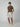 A young man stands against a plain background, wearing PROJEK RAW MENS CARPENTER SHORTS in light gray, a fitted brown t-shirt, and off-white sneakers. He faces forward with a neutral expression and relaxed posture.