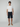 A young man faces forward against a light gray background, wearing a plain white t-shirt, PROJEK RAW MENS DRAWSTRING CHINO SHORT in navy blue (relaxed fit), and tan slip-on shoes.