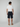A man faces away from the camera, wearing a white T-shirt and PROJEK RAW MENS DRAWSTRING CHINO SHORT in dark navy with tan slip-on shoes, standing against a plain light gray background.
