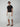 A man in a black t-shirt, PROJEK RAW MENS CARGO LINEN CAPRI SHORT with multiple pockets, brown sandals, and sunglasses stands against a plain gray background.
