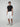A young man stands against a plain background, wearing a black t-shirt, PROJEK RAW MENS CARGO CAPRI SHORT in white with a belt, and gray and white sneakers. He faces forward with a neutral expression, showcasing versatile casual style.