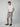 A man poses against a plain background wearing PROJEK RAW MENS CARGO CAPRI SHORTS, a white t-shirt, black belt, and black slip-on shoes. One hand is in his pocket as he smiles slightly.