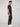 A young man with curly hair stands in profile against a plain light background, wearing a navy blue t-shirt, PROJEK RAW MENS 5-POCKET SOLID BUNGEE PANT with an elastic waistband, and white sneakers, looking straight ahead neutrally.