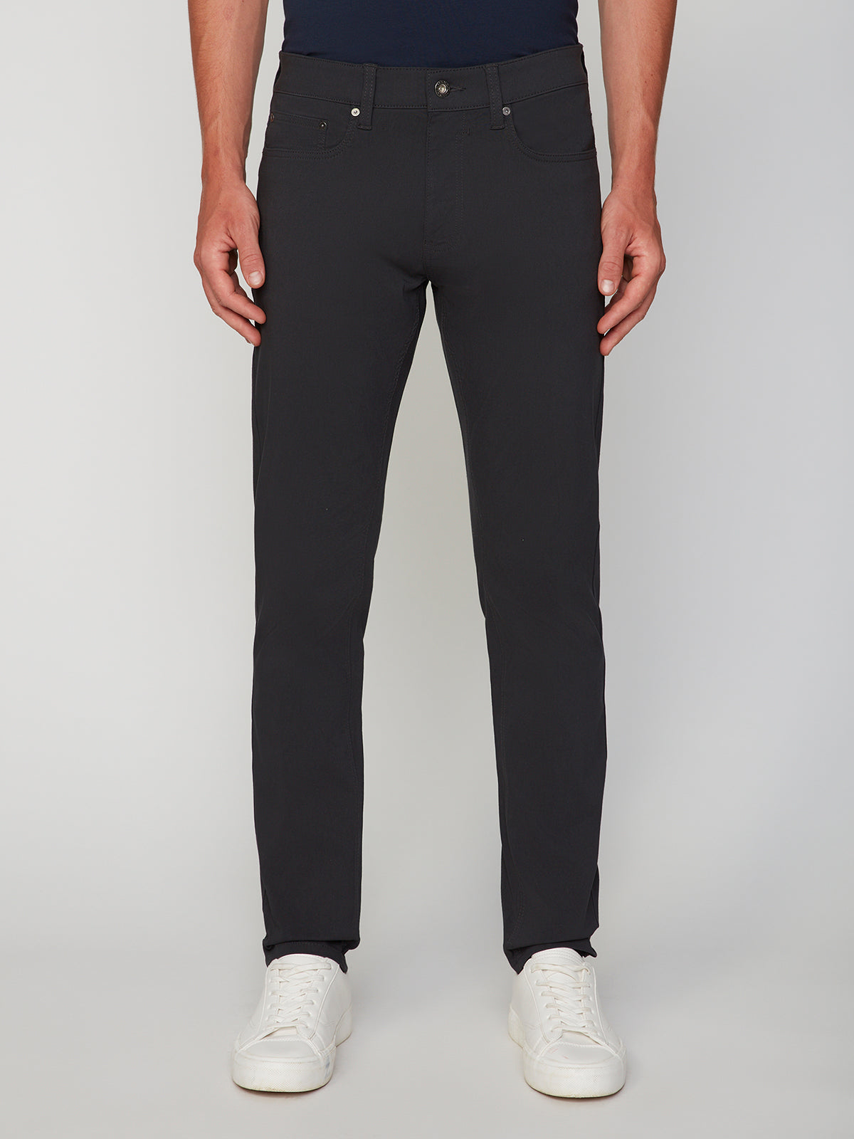 A person showcases the PROJEK RAW MENS 5-POCKET SOLID BUNGEE PANT with white sneakers against a plain light background, focusing on the lower torso and legs.