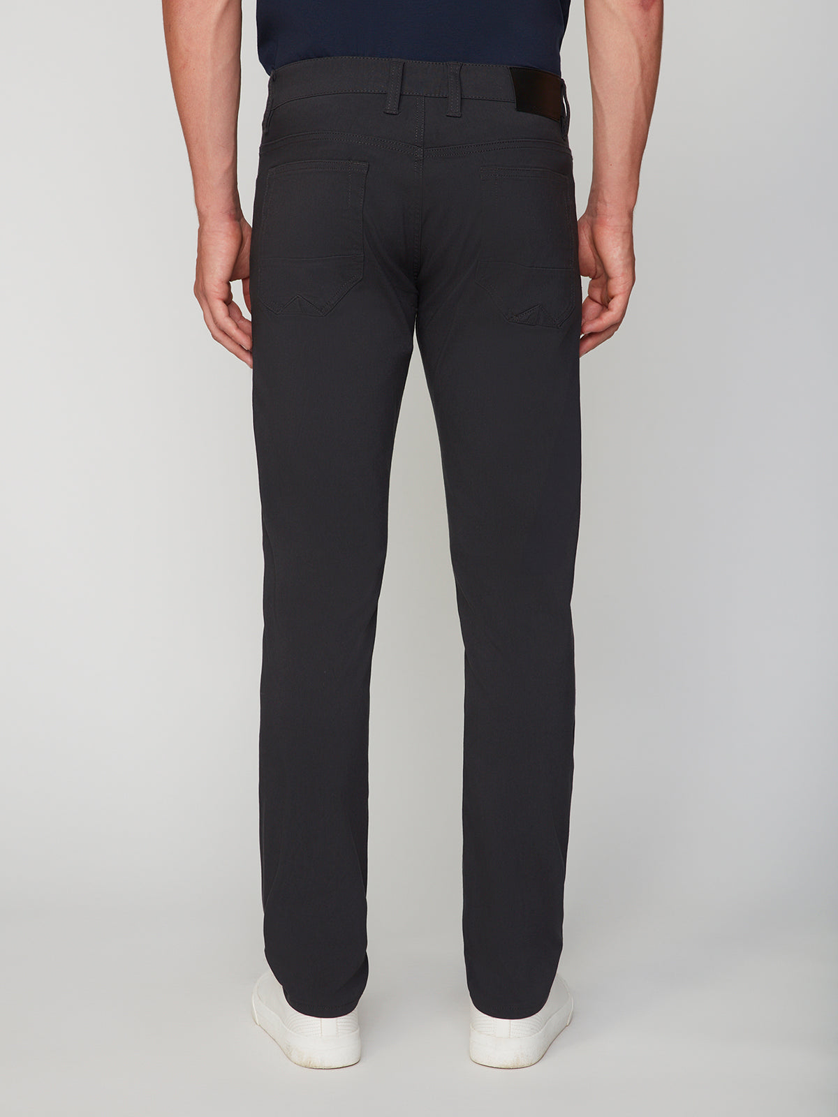 A person wearing PROJEK RAW MENS 5-POCKET SOLID BUNGEE PANT with a black belt and white sneakers stands facing away from the camera against a plain light background.