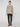 A person stands against a plain light background wearing PROJEK RAW MENS 5-POCKET SOLID BUNGEE PANT in dark green, paired with a beige zip-up cardigan and brown shoes. They face forward with a neutral expression and relaxed posture.
